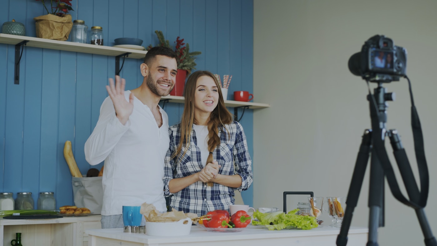 Couple waves at camera while filming in kitchen